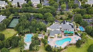 Vista aérea de una zona residencial con una gran piscina, canchas de tenis y abundante vegetación.