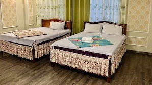 Une chambre d’hôtel avec deux lits simples, un plancher en bois, des couvre-lits à motifs floraux et une grande fenêtre avec des rideaux à motifs.