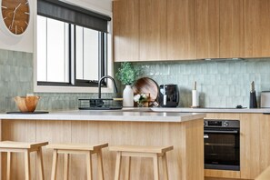 A modern kitchen with wooden cabinets, a built-in oven, and a window with blinds. - Bella Vita (Lorne)