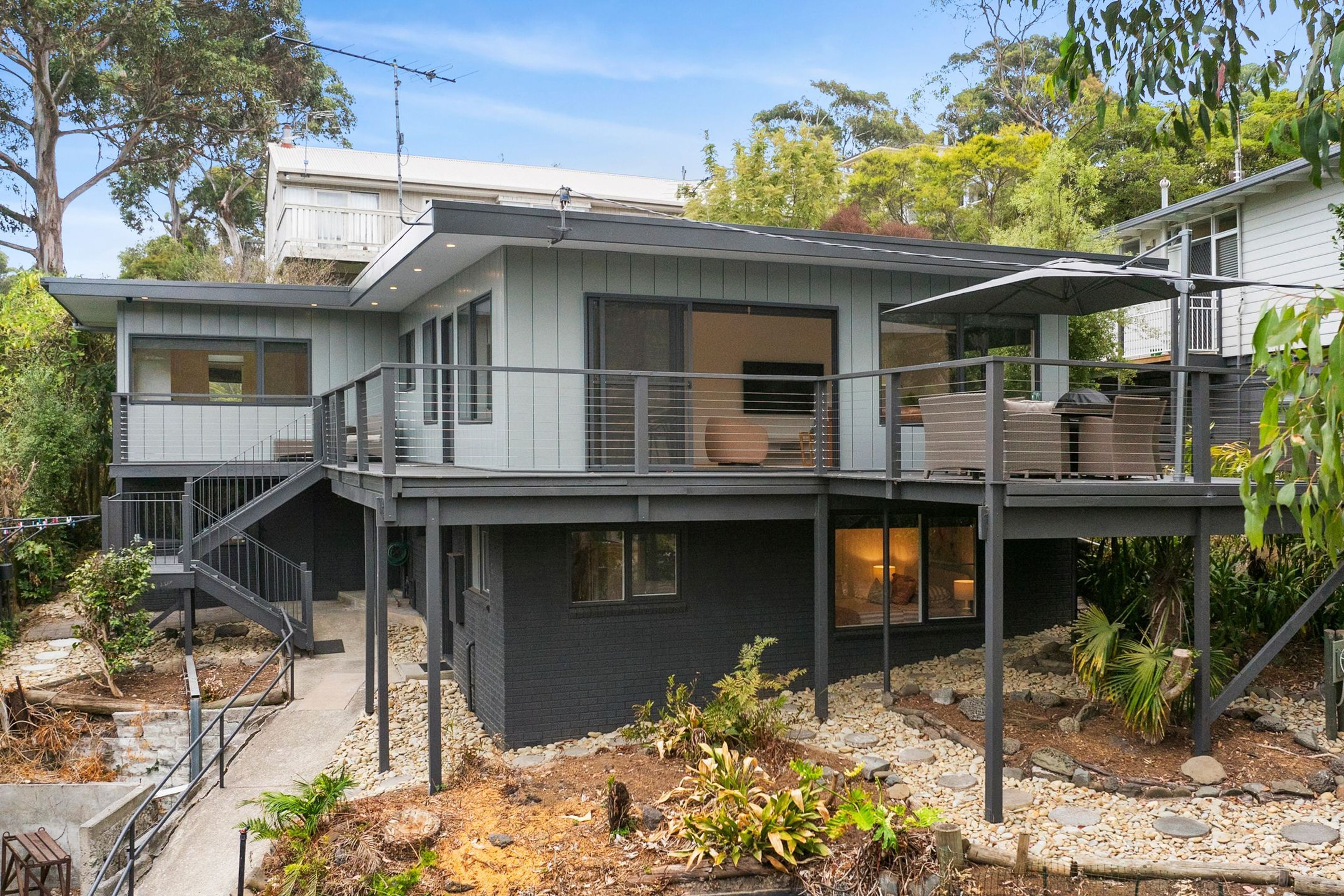 A modern two-story house with a balcony, a staircase, and a garden area.