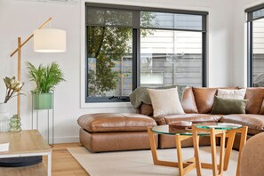 A modern living room with a leather sofa, a glass coffee table, and a floor lamp. - Bella Vita (Lorne)