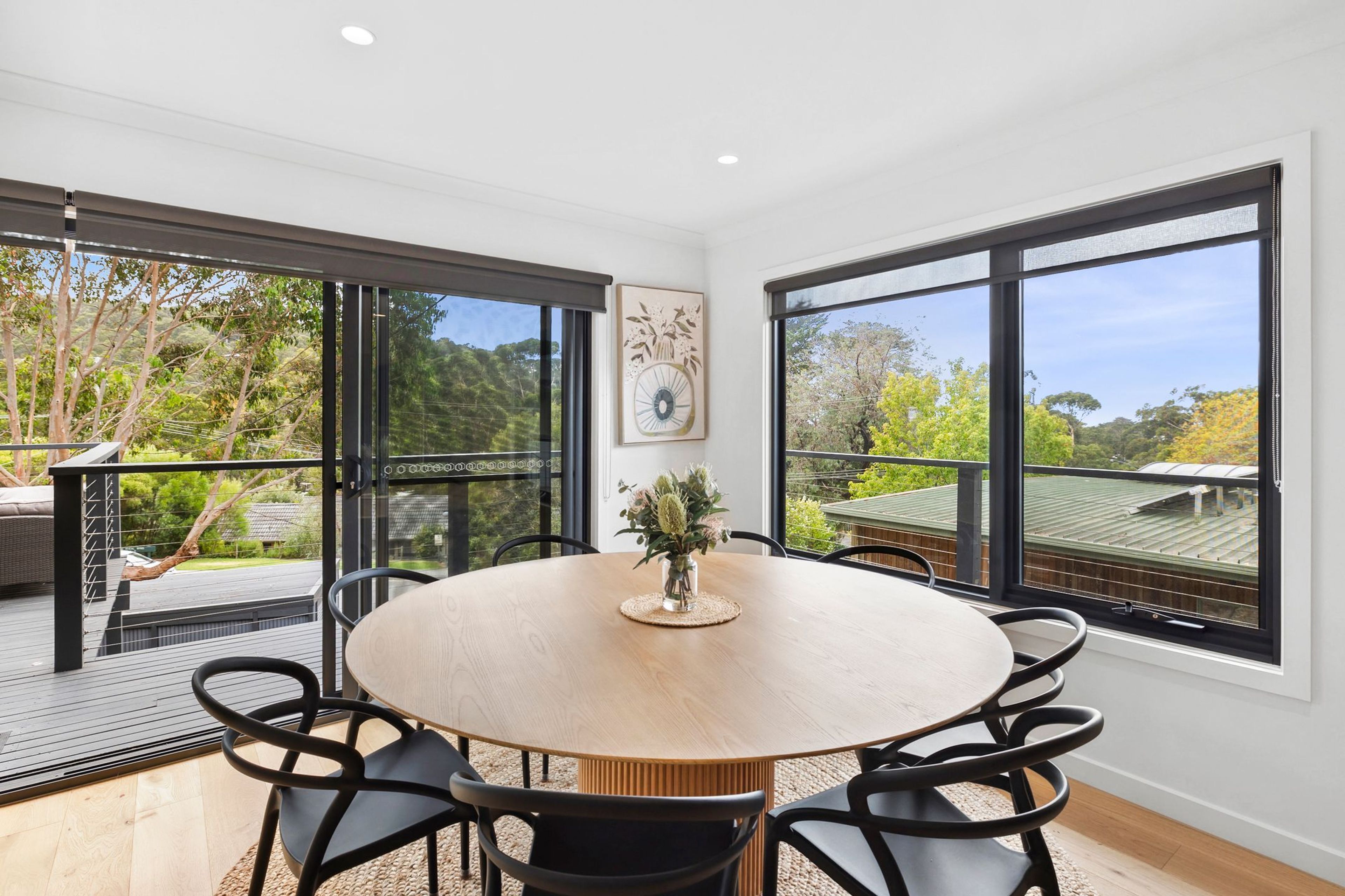 A modern dining area with a round table, black chairs, and a view of the outdoors through large windows.
