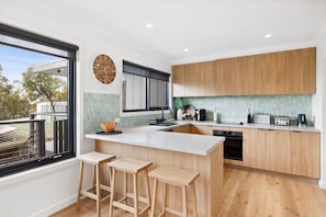 A modern kitchen with a large island, wooden cabinets, and a view of the outdoors. - Bella Vita (Lorne)