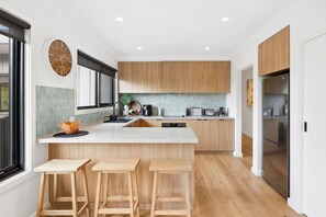 A modern kitchen with wooden cabinets, a central island with stools, a built-in oven, and a large window.