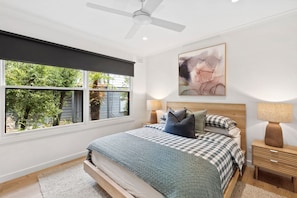 A bedroom with a bed, two bedside lamps, a ceiling fan, a window with a view of greenery, and a wall-mounted abstract painting. - Bella Vita (Lorne)