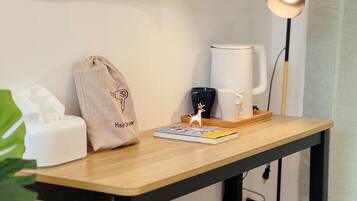 A small wooden table with a coffee maker, a mug, a book, a hairdryer bag, and a lamp.