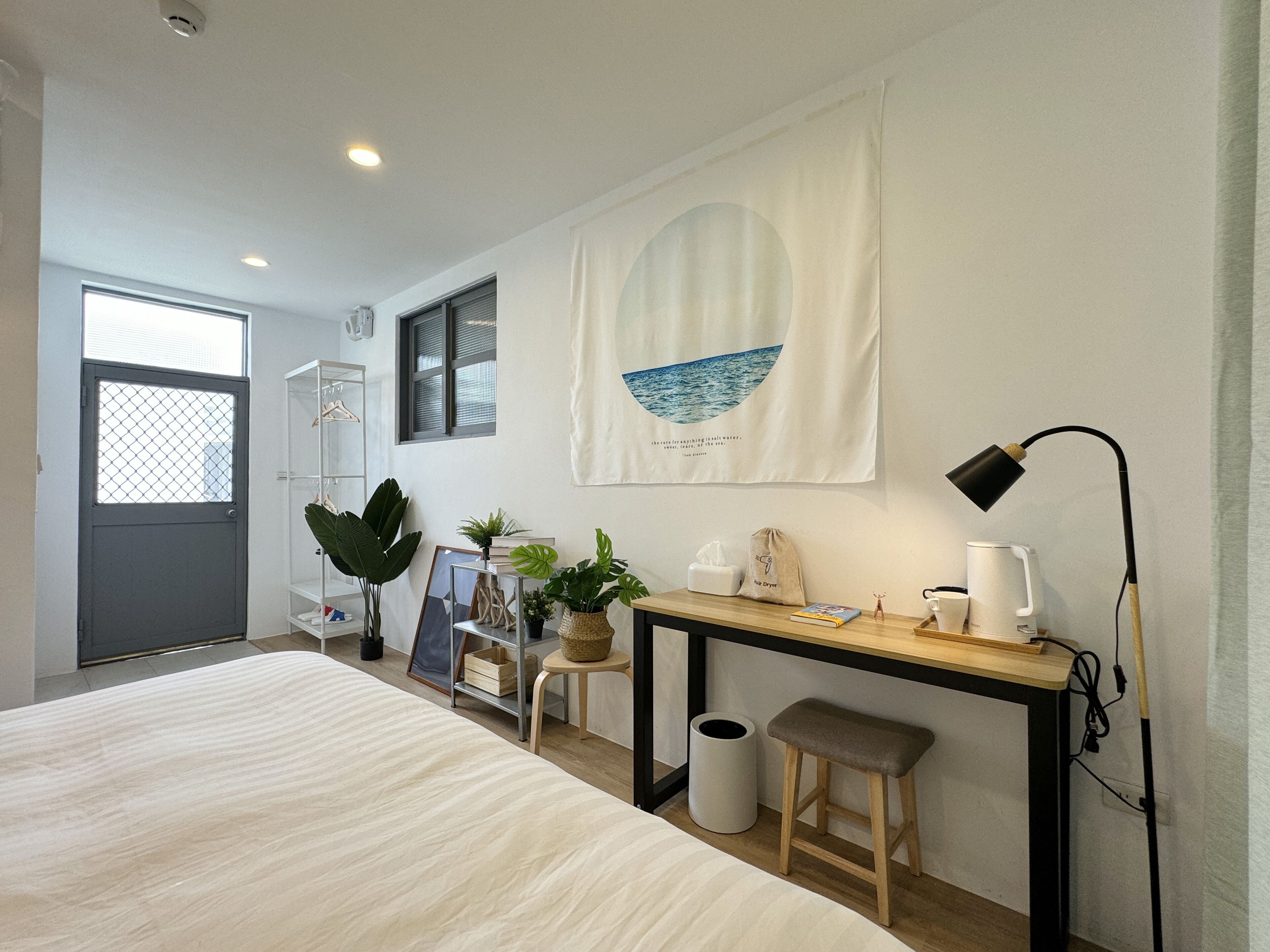 A bedroom with a bed, a desk, a chair, a waste bin, and a window.