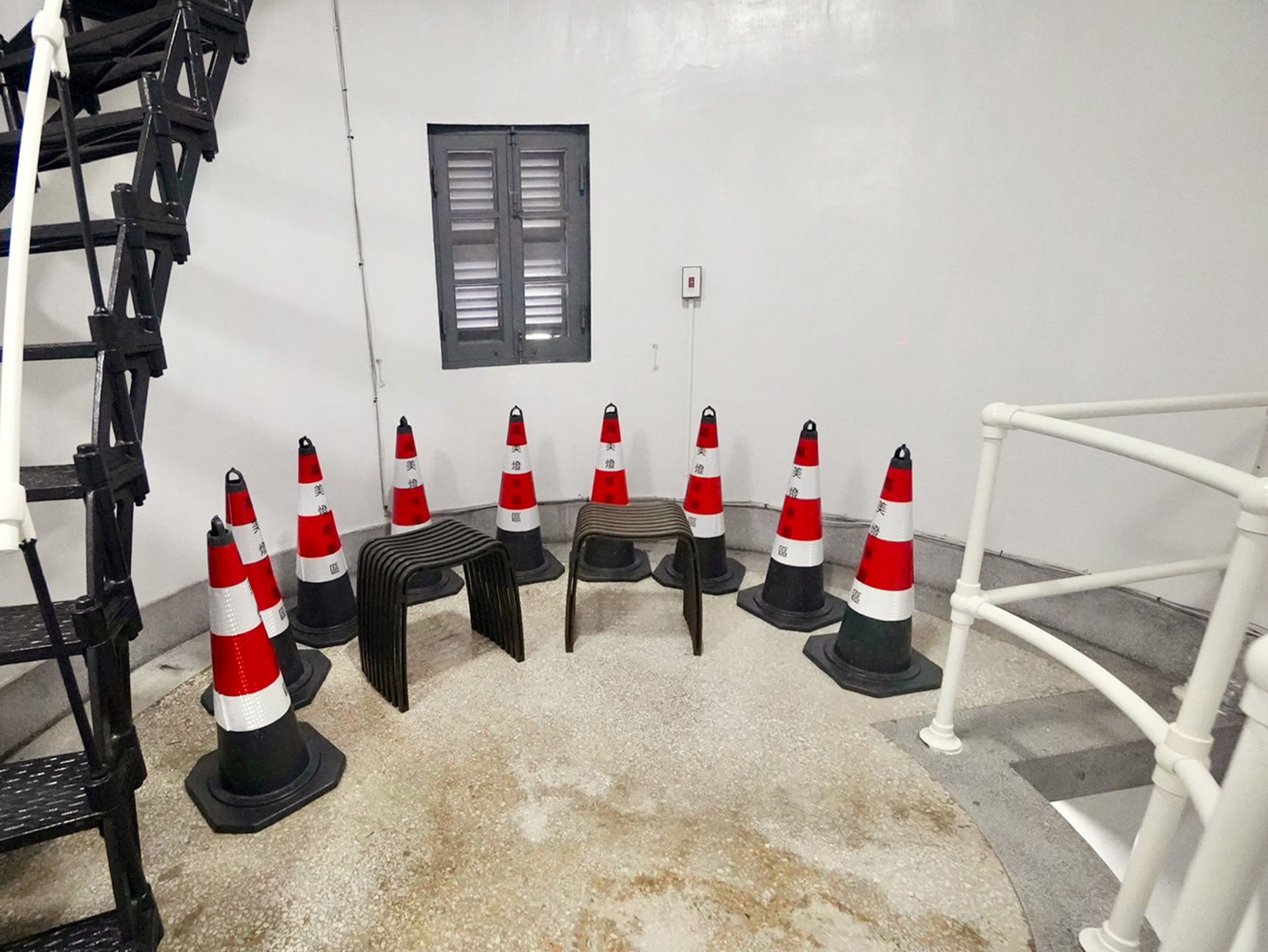A staircase with black railings, a small table, and several traffic cones arranged in a circle.