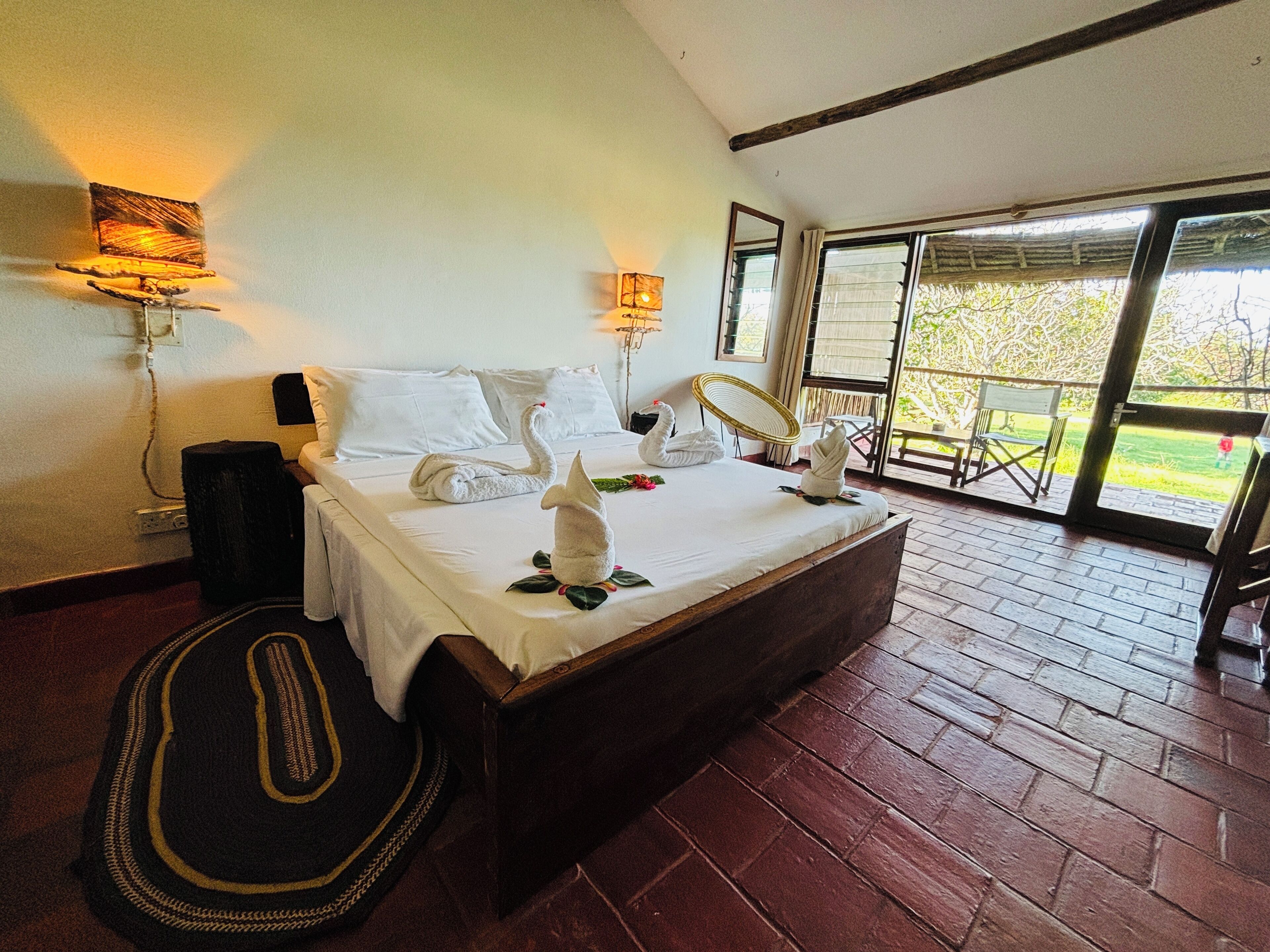 A spacious bedroom with a large bed, two wall-mounted lamps, and a view of the outdoors through a sliding glass door.