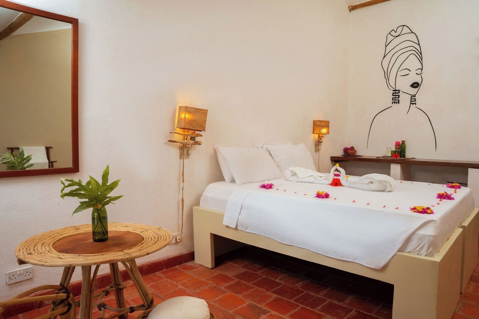 A bedroom with a bed, bedside tables, a mirror, a wall-mounted lamp, and a wall art piece.