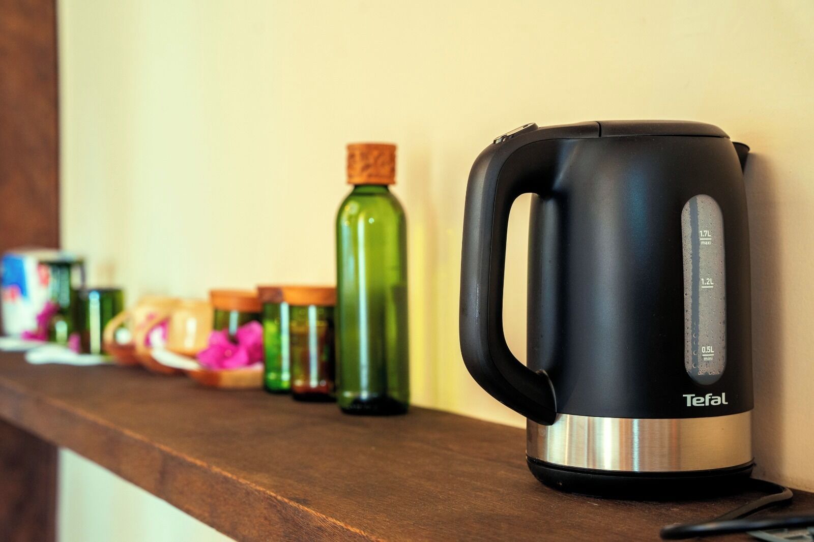 Una cocina con una tetera Tefal negra sobre un estante de madera, rodeada de varios recipientes y frascos de vidrio.