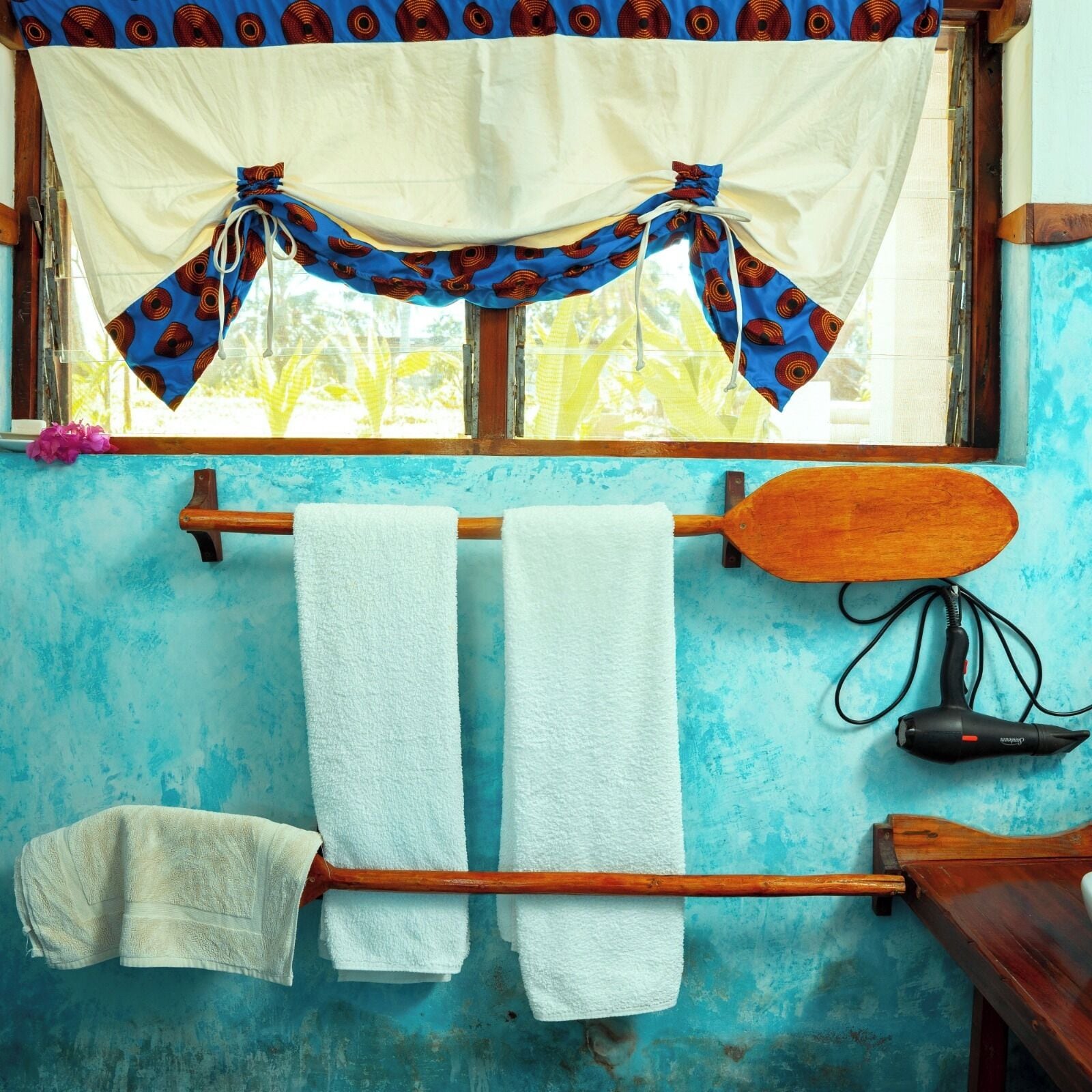 A bathroom with a blue wall, a wooden towel rack with two towels, a wooden paddle, and a hairdryer.