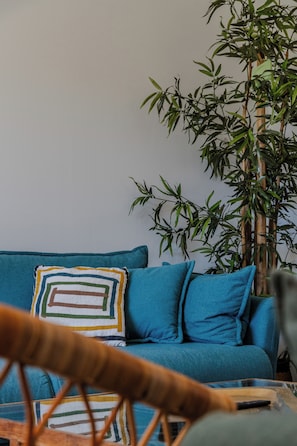 Una habitación con un sofá azul, una planta de bambú y una silla de fibras naturales.