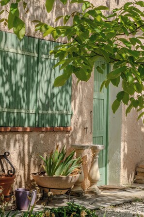 A rustic building with a green shutter, a door, and potted plants.