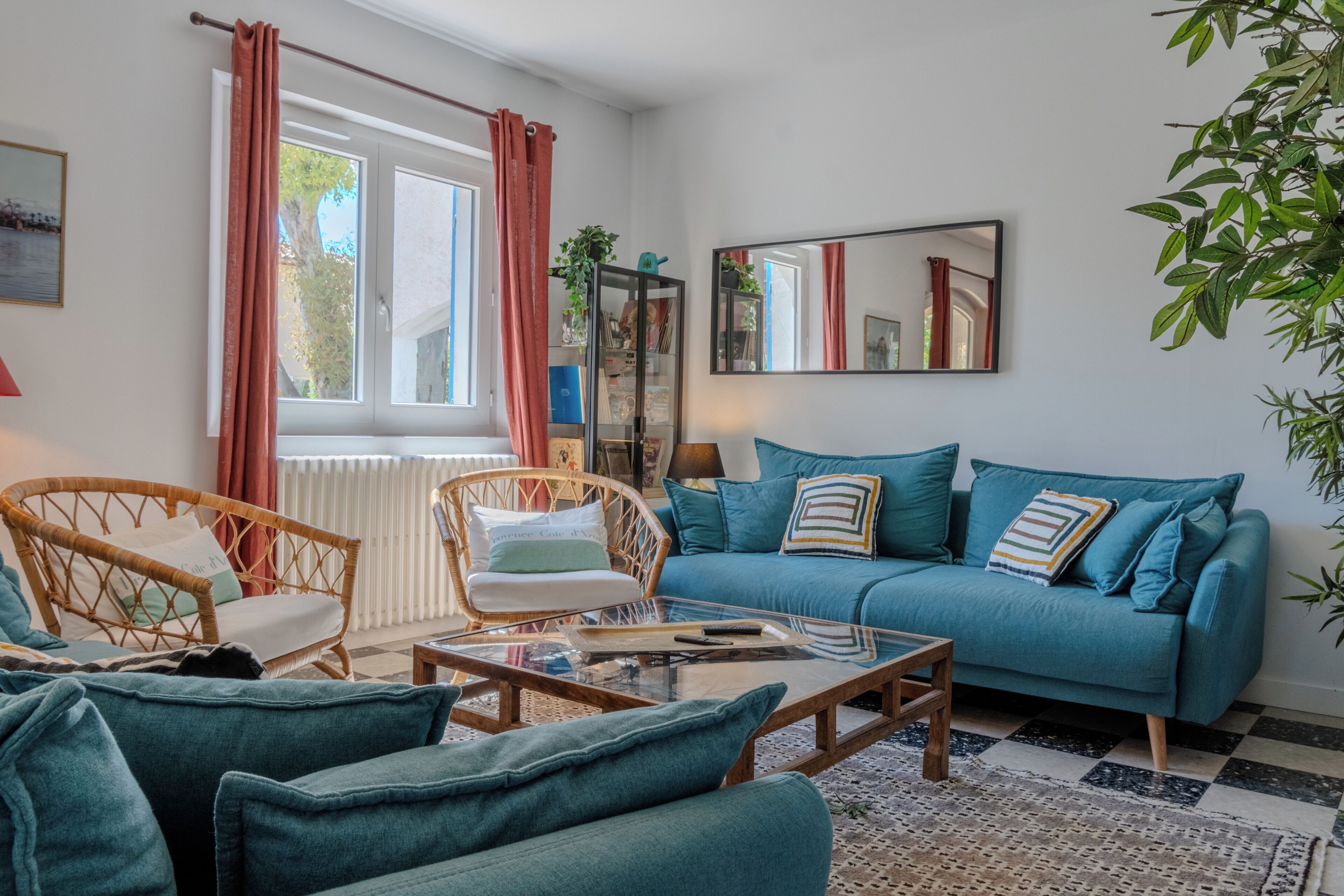 A living room with a blue sofa, a glass coffee table, wicker chairs, a radiator, and a large mirror on the wall.