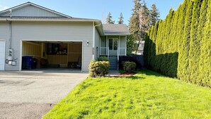 A single-story house with a garage open, a well-maintained lawn, and a tall hedge. - Family-Friendly Retreat in Marysville (Marysville)