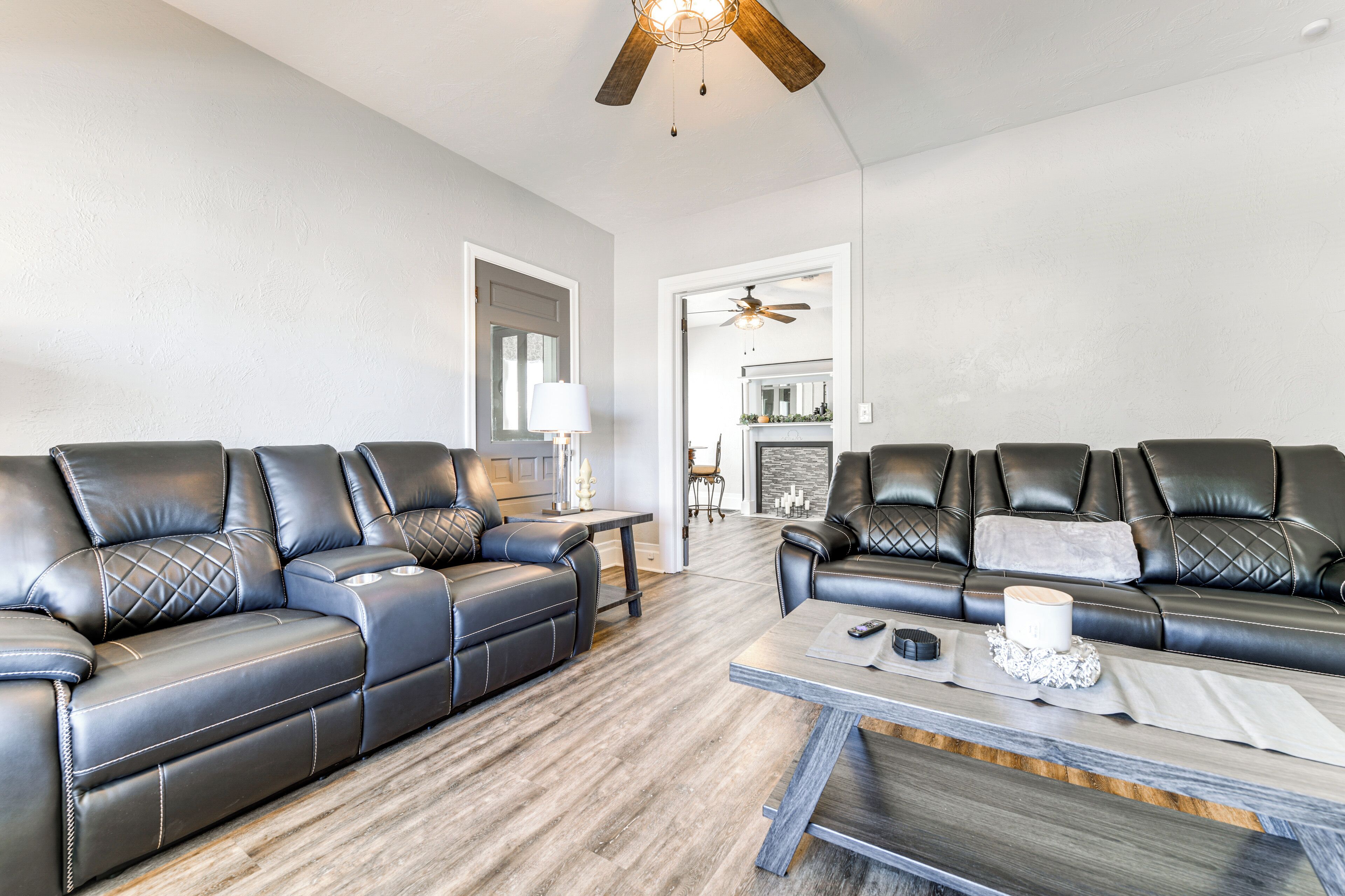 Un salon moderne avec deux canapés en cuir noir, une table basse en bois et un ventilateur de plafond.