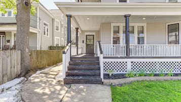 Une maison à deux étages avec un porche à l’avant, un escalier menant à l’entrée et un petit jardin.