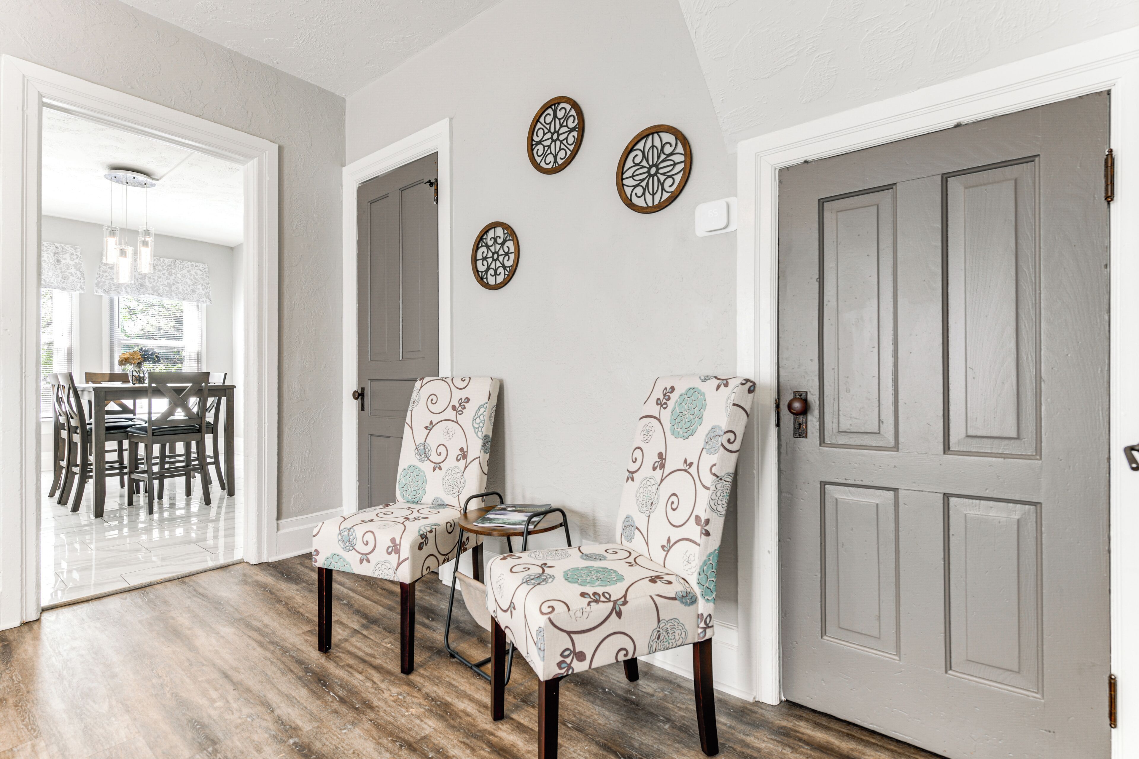 Un couloir avec deux fauteuils rembourrés, une petite table et des œuvres d’art décoratives accrochées au mur.