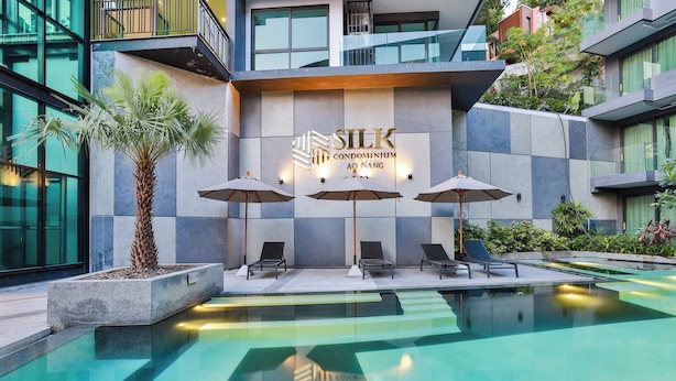 A modern building with a sign reading "SILK Condominium AO NANG" and a pool area with lounge chairs and umbrellas.