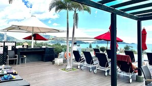 Eine Terrasse im Freien mit Liegestühlen, Sonnenschirmen und Grillbereich.