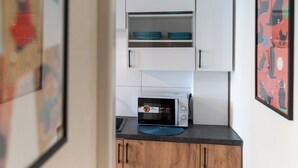 Une petite cuisine équipée avec des meubles blancs, un four à micro-ondes et un tapis bleu sur le plan de travail.