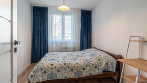 Une chambre avec un lit en bois, une fenêtre avec des rideaux bleus et un luminaire suspendu.