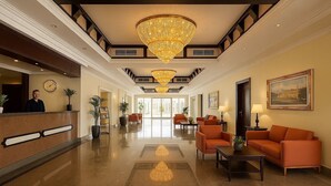 A spacious lobby with a grand chandelier, a reception desk, comfortable seating, and a large window offering a view. - FALAJ DARIS HOTEL (Nizwa)