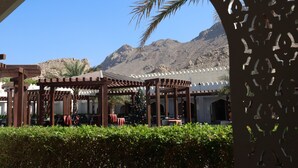 An outdoor seating area with wooden pergolas and tables, a Christmas tree, and a mountain backdrop. - FALAJ DARIS HOTEL (Nizwa)