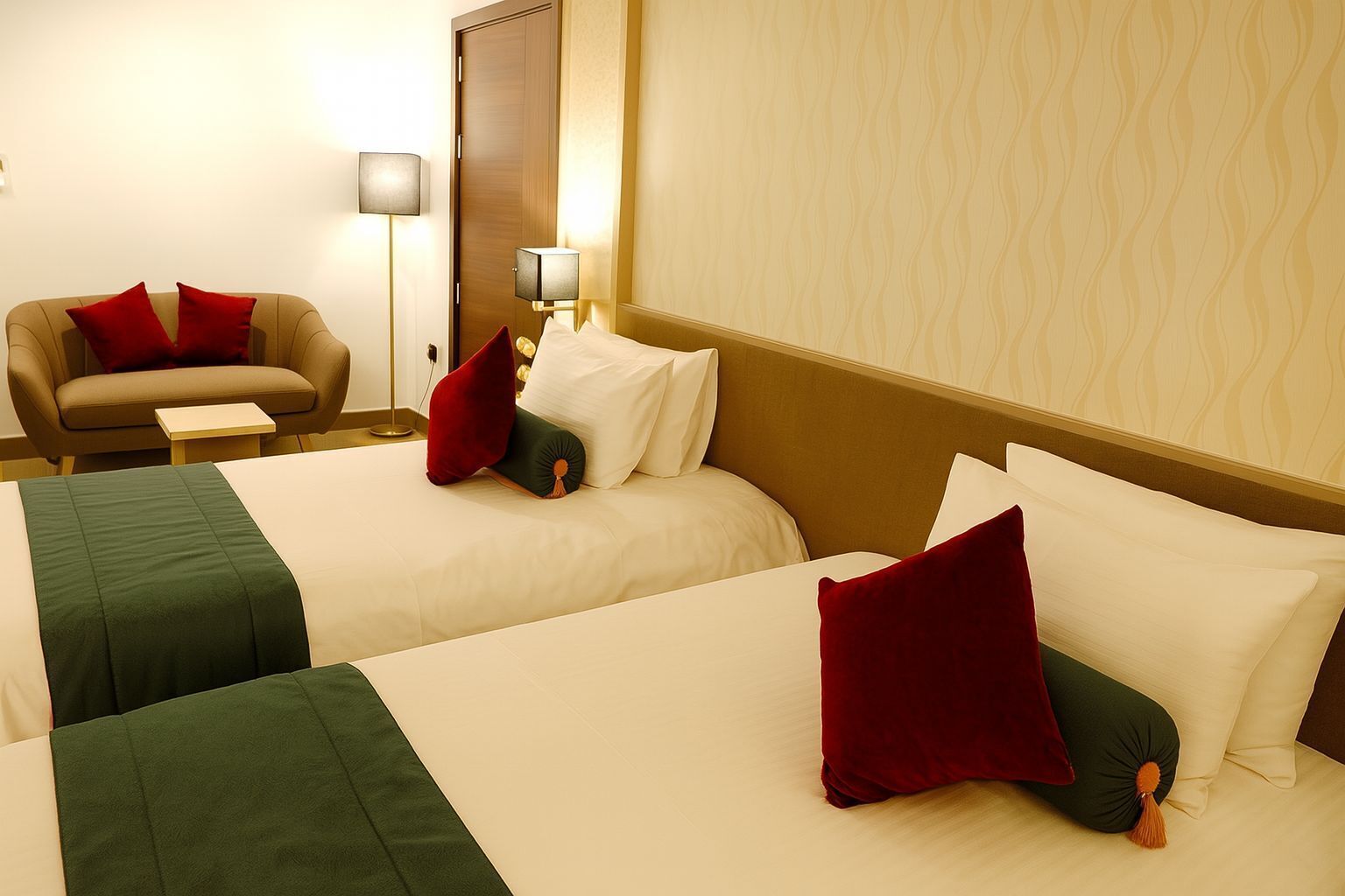 Ett hotellrum med två sängar, båda med vita sängkläder och röda kuddar. Det finns en soffa med en röd prydnadskudde och ett litet bord bredvid. En golvlampa syns i hörnet.