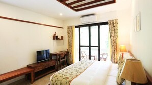 A hotel room with a bed, a desk with a TV, a window with curtains, and a lamp. - Aranya Nivas Resort (Samakhunta)