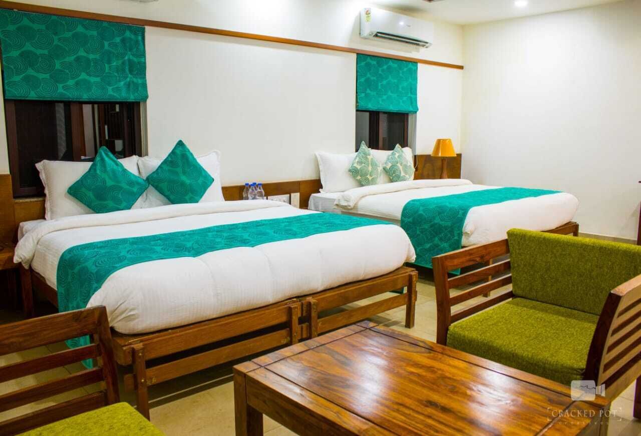 A hotel room with two beds, wooden furniture, and a green chair.