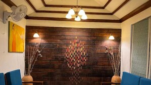 A room with a wooden wall, blue sofas, a wooden coffee table, and a decorative wall piece. - Aranya Nivas Resort (Samakhunta)