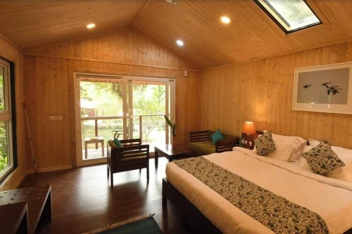A wooden room with a bed, a bench, a table, and a door leading to an outdoor area.