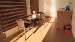 A small, sunlit room with a round table and wicker chairs, a wooden cabinet, and a red trash bin. - La Paz Resort By Shikhar Hospitality (Nainital)