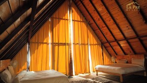 A cozy attic bedroom with two beds, wooden beams, and large windows with curtains. - La Paz Resort By Shikhar Hospitality (Nainital)