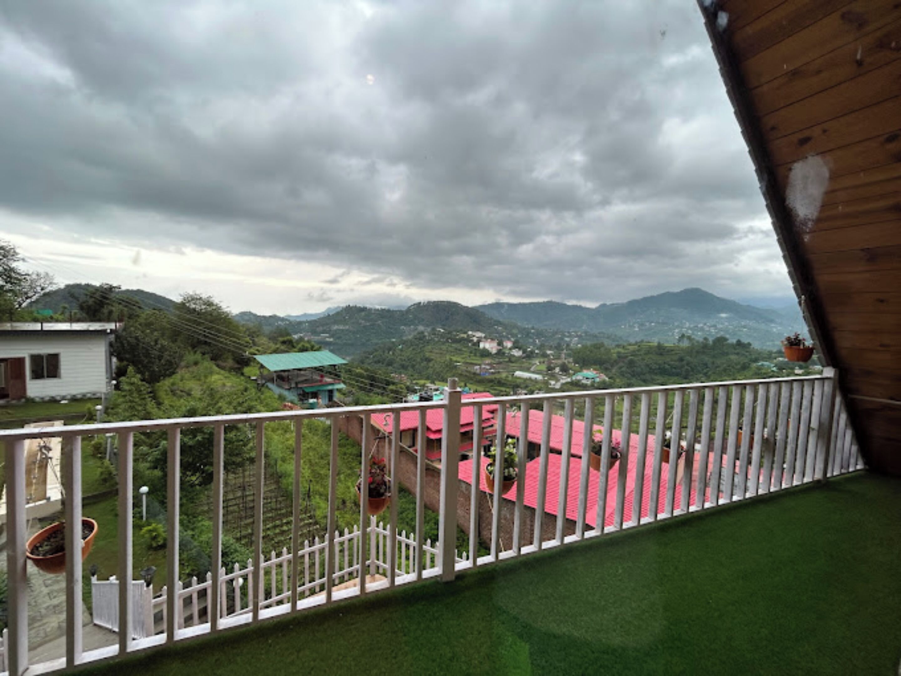 Un balcone con ringhiera bianca che si affaccia su un paesaggio verde con edifici e montagne.