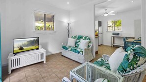 A living room with a television, wicker furniture, and a kitchen area with a microwave. - "The Little Blue Shack" - Marcoola Granny Flat (Bli Bli)