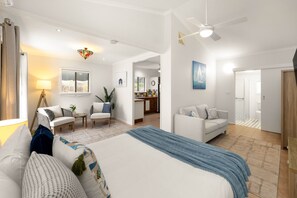 Amplia habitación de hotel con una cama grande, un rincón de estar con una silla y una mesa, una kitchenette y un baño.