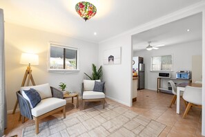 Un salon moderne avec un canapé, un fauteuil et une petite table sur laquelle se trouve une lampe. Il y a également un coin cuisine équipé d’un réfrigérateur, d’un four à micro-ondes et d’une table à manger.