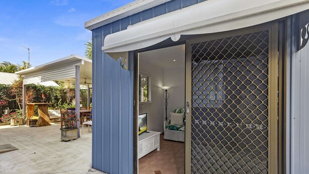 A modern house with a blue exterior, a sliding glass door leading to a bedroom with a bed, a nightstand, and a lamp. - "The Little Blue Shack" - Marcoola Granny Flat (Bli Bli)