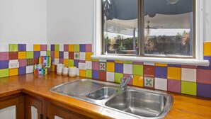 A kitchen with a double sink, colorful tiles, and a window overlooking a garden. - "The Little Blue Shack" - Marcoola Granny Flat (Bli Bli)