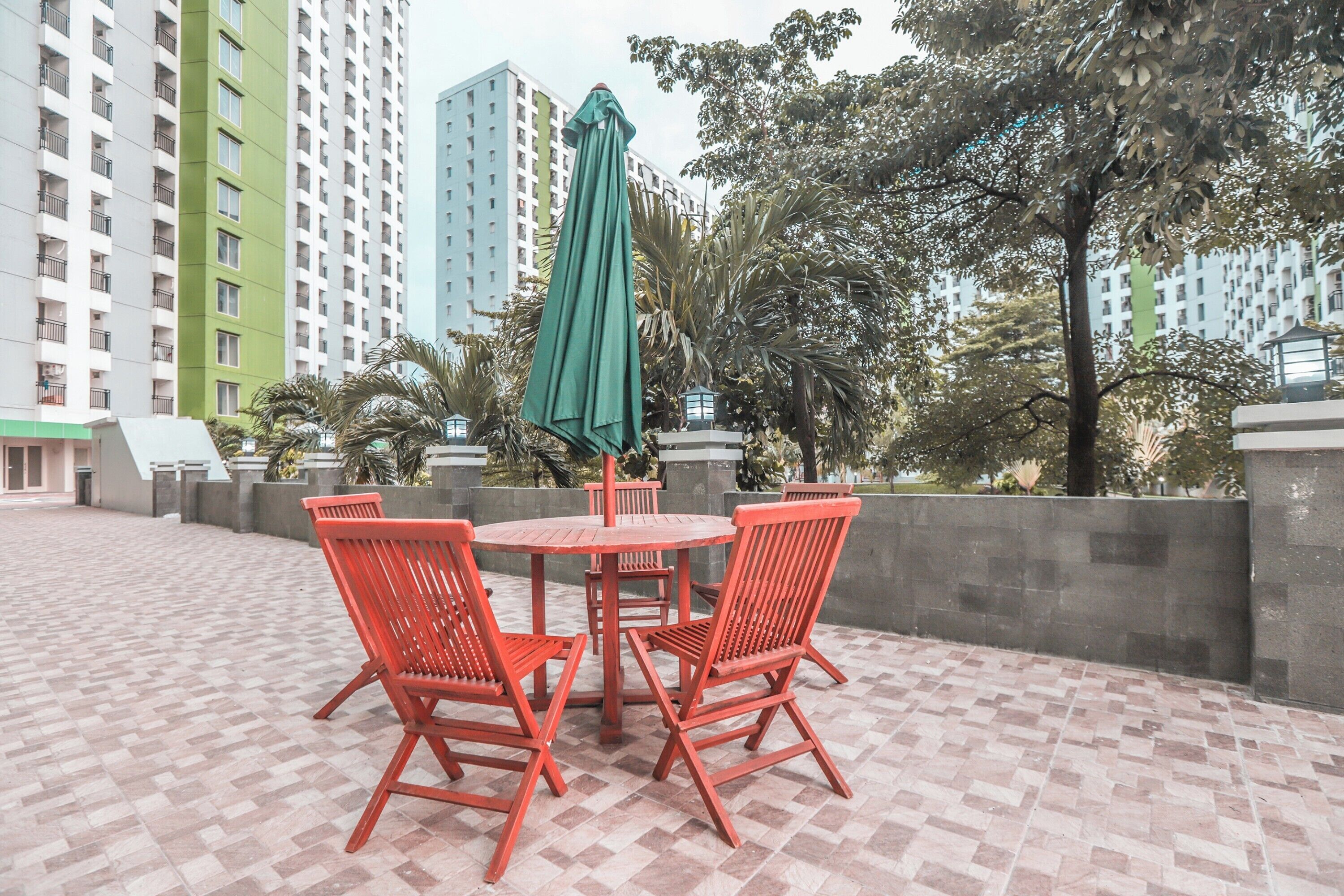Un patio con una mesa redonda y cuatro sillas rojas, rodeado por un muro de ladrillo bajo.