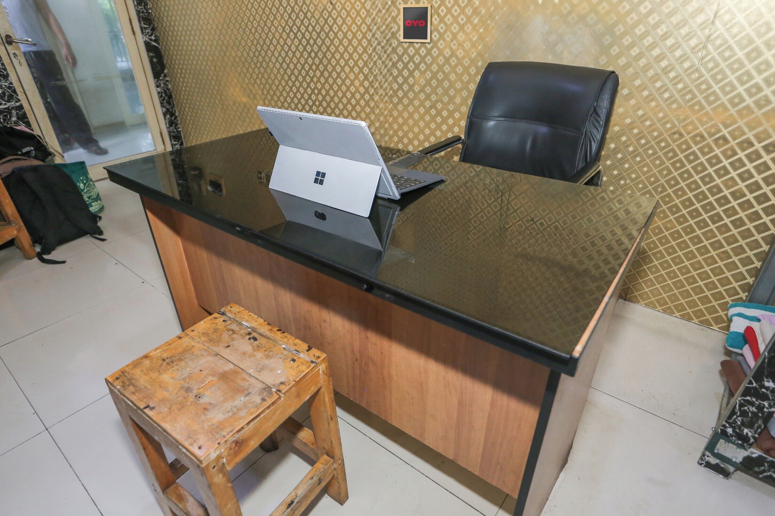 Mostrador de recepción con una computadora portátil, un taburete de madera y una silla de oficina negra.