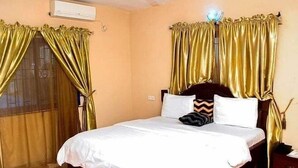 A hotel room with a bed, curtains, and a nightstand. - Star Rise Golden International Hotel  (Badagry)