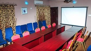 A conference room with a long table, blue and pink chairs, patterned curtains, a projector screen, and a ceiling fan. - Star Rise Golden International Hotel  (Badagry)