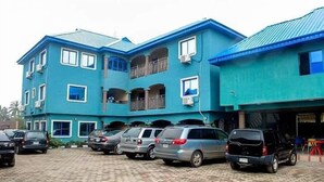 A multi-story building with a blue exterior, a parking area with several cars, and a balcony on the upper floor. - Star Rise Golden International Hotel  (Badagry)