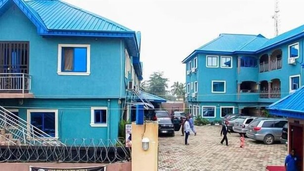 A blue building with multiple windows and balconies, surrounded by a parking area with cars. - Star Rise Golden International Hotel  (Badagry)