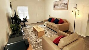 Un salon avec un canapé beige, une table basse, un téléviseur et un ventilateur de plafond.