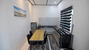 A compact kitchen with a wooden table, black chairs, a refrigerator, and a window with blinds.